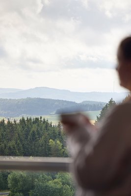 Frau genießt den Ausblick auf die Eifel vom Zimmer im Nürburgring Hotel mit einer Tasse in der Hand