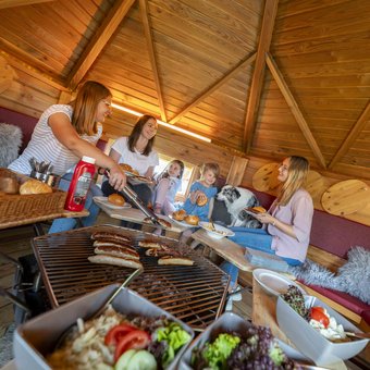 Familie grillt gemeinsam in einer Holzhütte im Nürburgring Ferienpark, gemütliche Atmosphäre mit Kindern und Hund