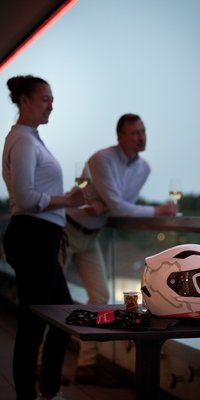 Paar mit Wein auf dem Balkon im Nürburgring Hotel, Motorsporthelm im Vordergrund