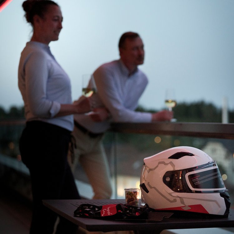 Paar mit Wein auf dem Balkon im Nürburgring Hotel, Motorsporthelm im Vordergrund