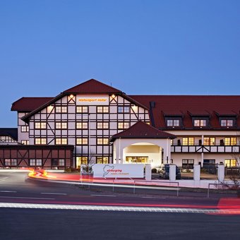 Außenansicht des Nürburgring Motorsport Hotels in der Abenddämmerung mit beleuchteter Fassade und Parkplatz.
