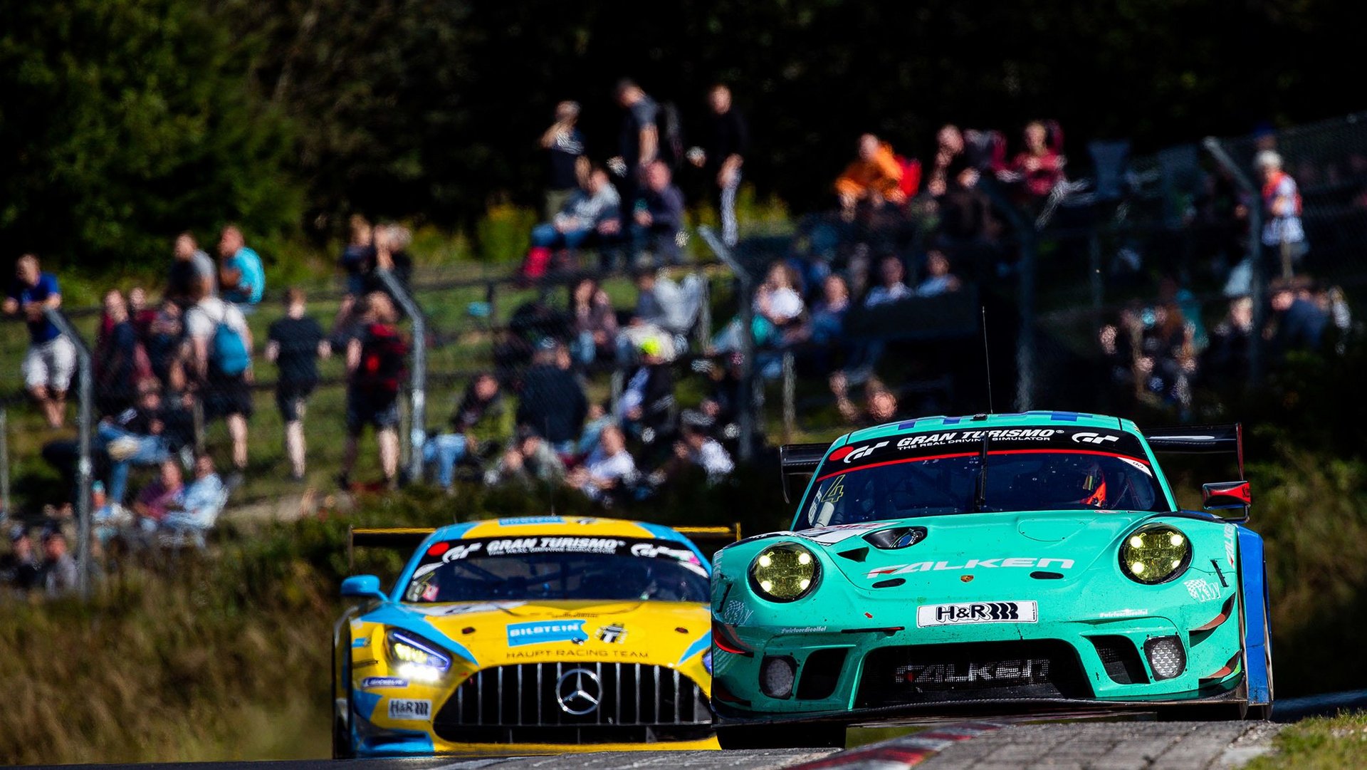 Rennwagen auf der Nordschleife bei der ADAC Nürburgring Langstrecken-Serie mit jubelnden Fans am Streckenrand.