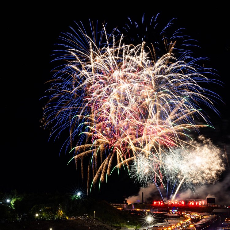 Feuerwerk über dem Nürburgring während eines großen Events mit Bühne und Besuchermenge.