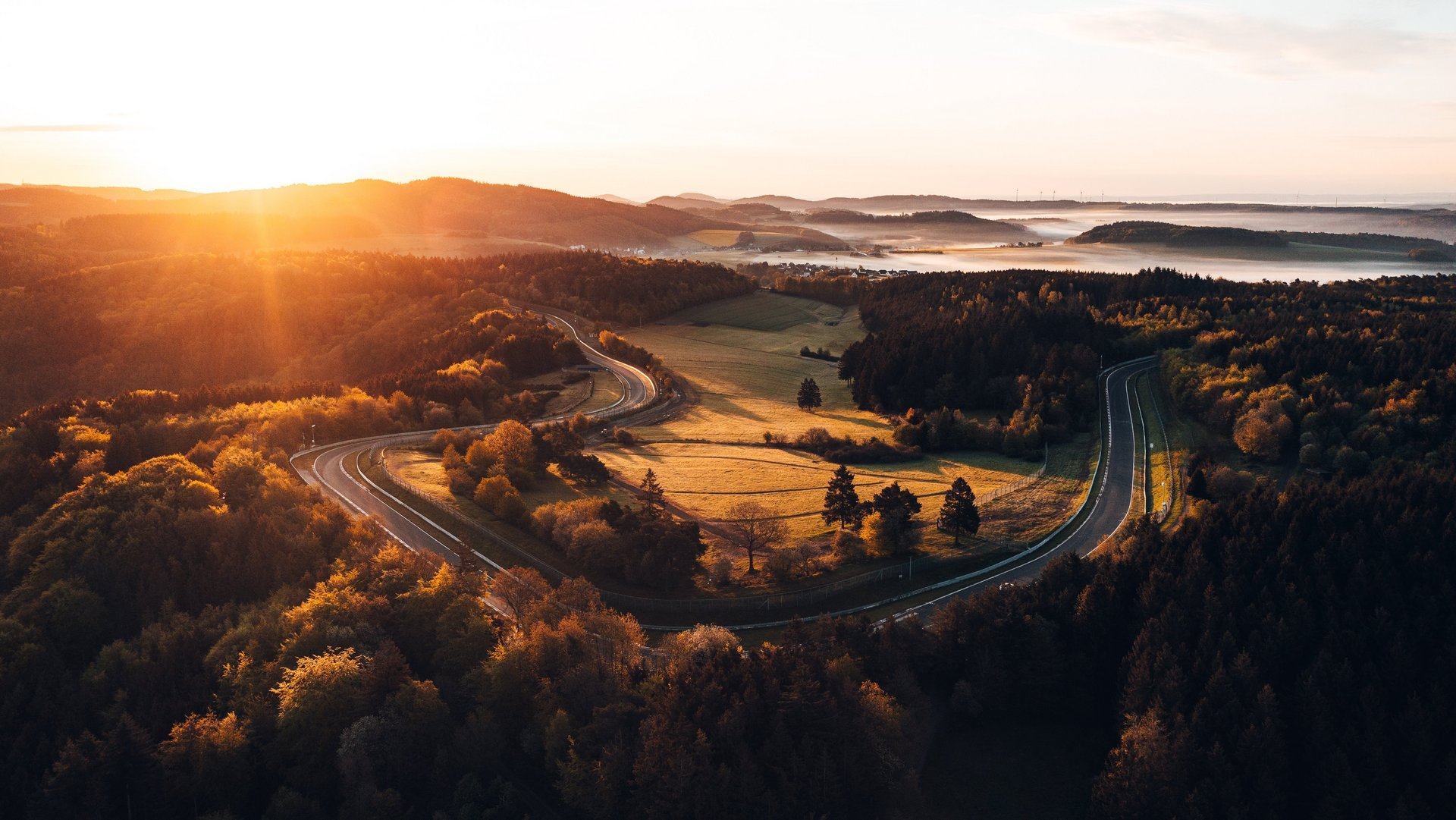 Luftaufnahme des Nürburgrings bei Sonnenaufgang – die legendäre Nordschleife schlängelt sich durch die herbstliche Landschaft der Eifel.