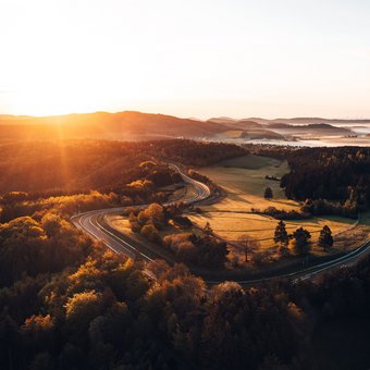 Luftaufnahme des Nürburgrings bei Sonnenaufgang – die legendäre Nordschleife schlängelt sich durch die herbstliche Landschaft der Eifel.